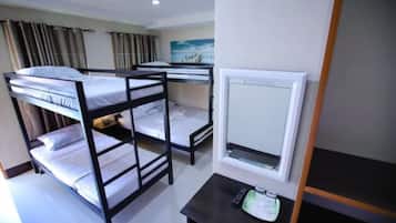 A dormitory room with bunk beds, a small table with a remote control, and a window with curtains.