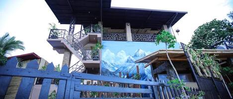 Un edificio con un mural de montaña, una valla de madera y un balcón con plantas.