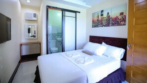 Une chambre d’hôtel avec un lit, une télévision, une salle de bain et un tableau représentant un paysage urbain accroché au mur.