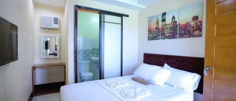 A hotel room with a bed, a television, a bathroom, and a cityscape painting on the wall.