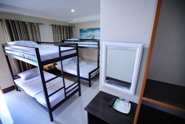 A dormitory room with bunk beds, a small table with a remote control, and a window with curtains. - Marcos Tourist Inn By Reddoorz (Ormoc)