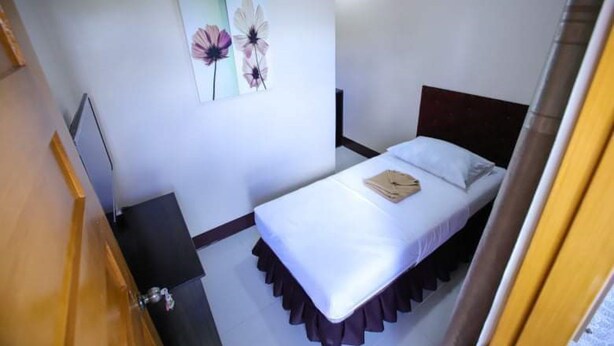 Une petite chambre à coucher, bien rangée, avec un lit simple, une table de chevet et une œuvre d’art accrochée au mur.