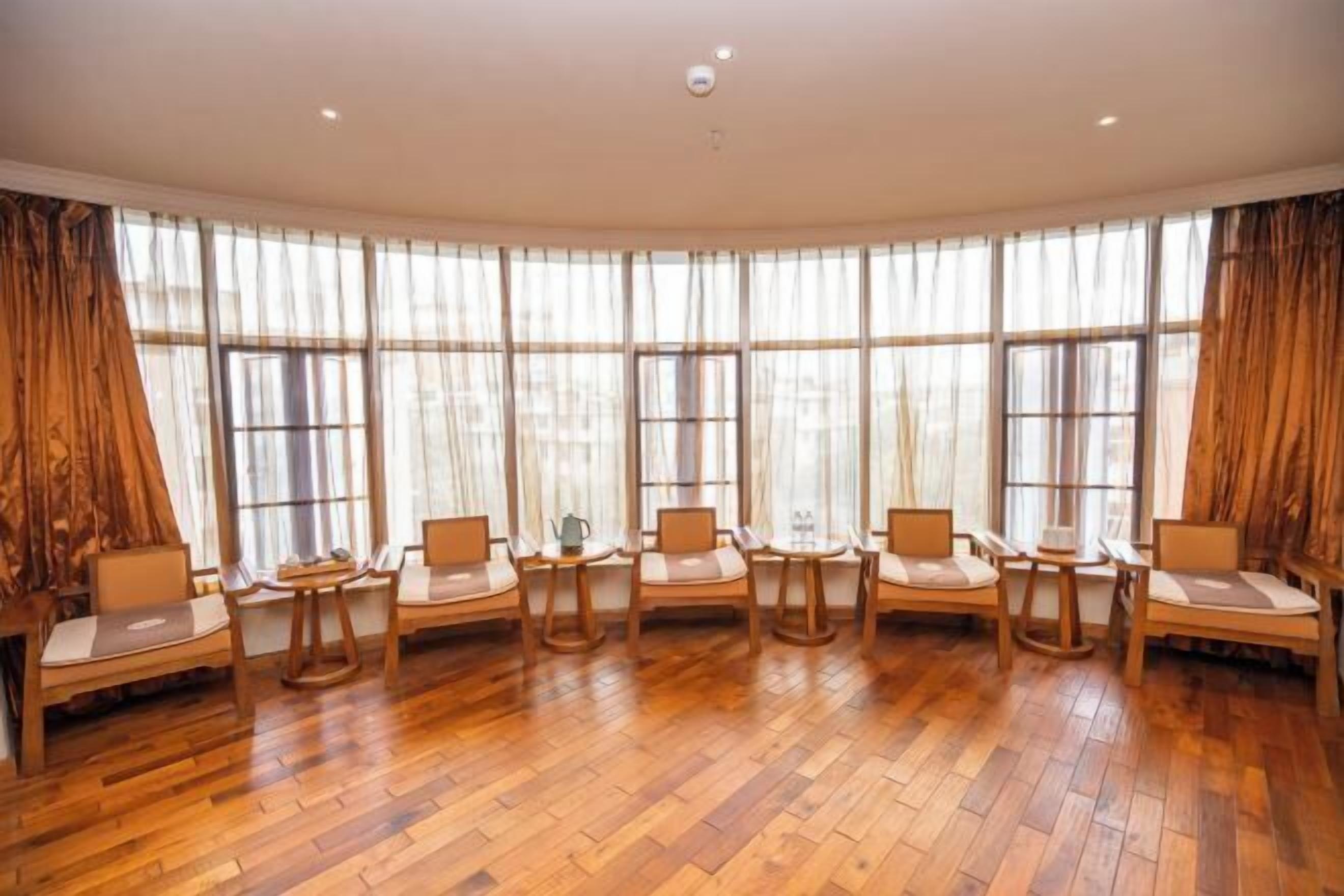 A room with a curved layout, large windows, wooden flooring, and multiple seating arrangements.