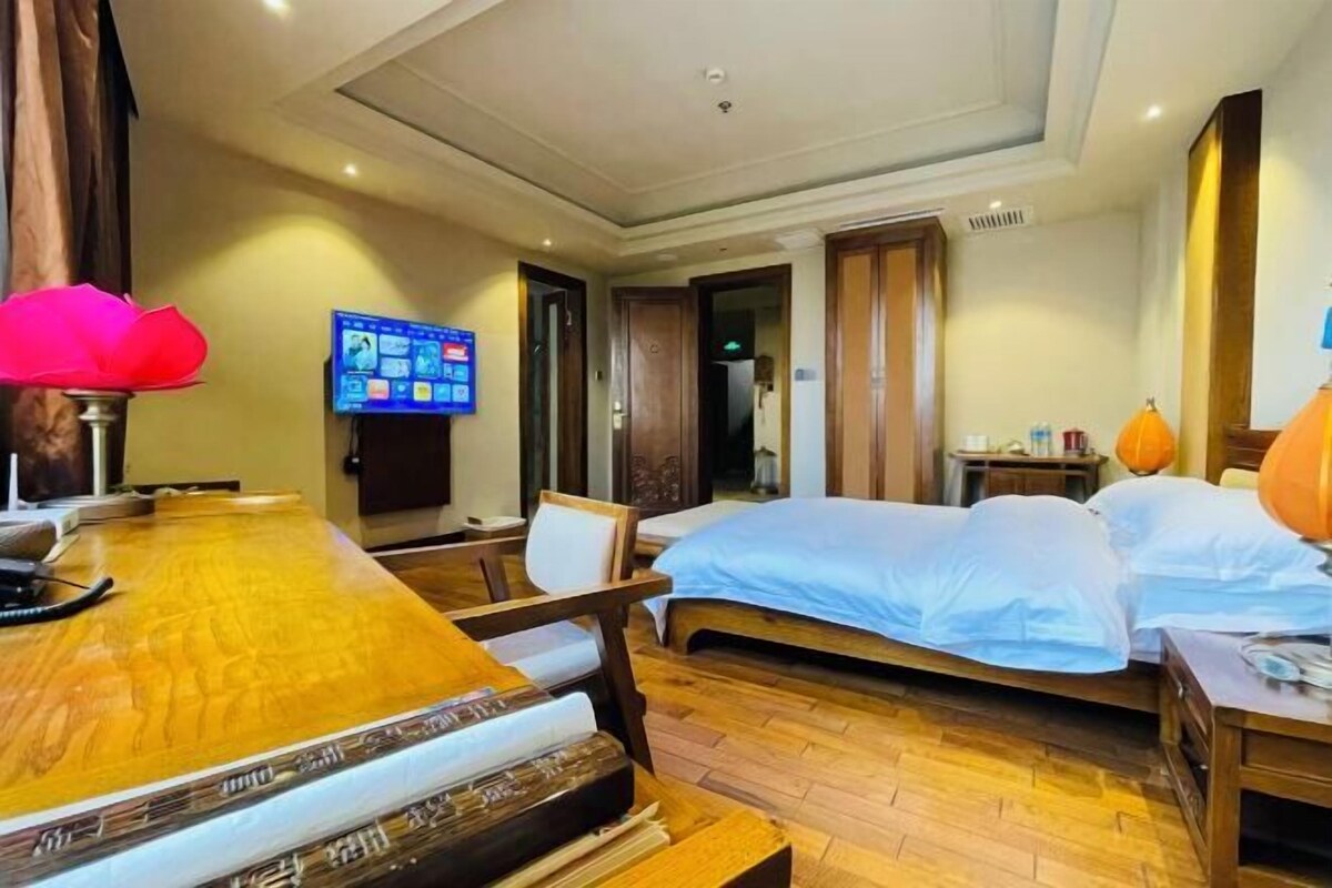 A hotel room with a wooden dining table, a bed with white bedding, a TV mounted on the wall, and a wooden floor.