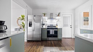 Una cocina moderna con un refrigerador de acero inoxidable, horno empotrado y microondas. Hay plantas en macetas y una cafetera en la encimera.