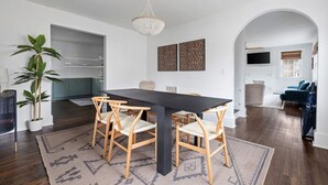 Un comedor moderno con una mesa oscura y sillas de madera clara, una lámpara de araña y vistas a la cocina.