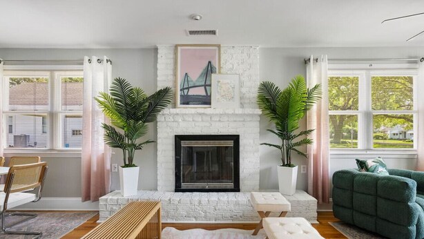 Una sala de estar con chimenea de ladrillo blanco, dos plantas en macetas, un sofá verde y un banco de madera.