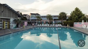 Una piscina con sillas de descanso y sombrillas, rodeada de edificios y árboles.