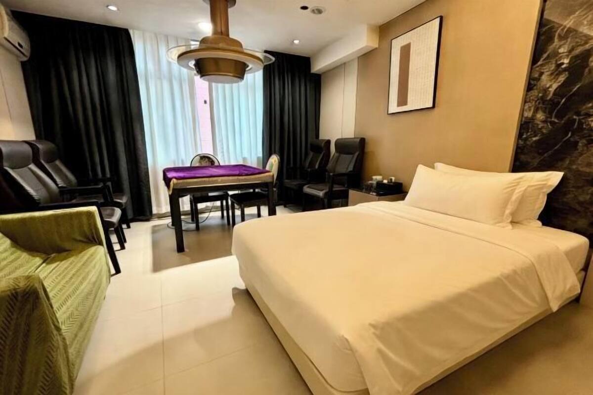 Habitació d'hotel amb un llit gran, escriptori amb cadira, sofà i finestra amb cortines.