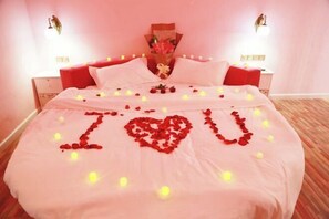 Una cama con pétalos de rosa formando la frase 'I love you' y un ramo de flores en la cabecera.
