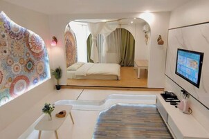 A modern hotel room with a bed, a small table, a TV, and a unique wall design.
