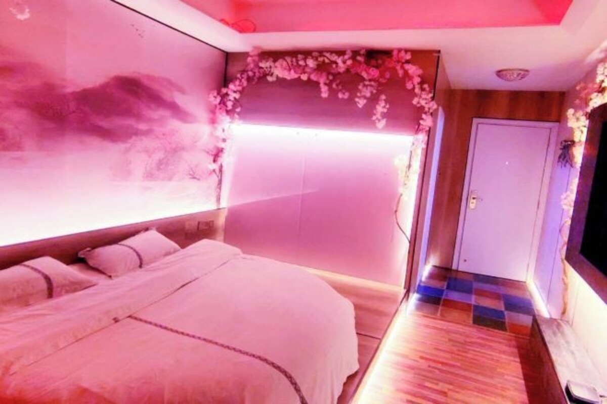 Un dormitorio con cama, televisor montado en la pared y una puerta.