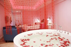 Una habitación con una bañera grande llena de pétalos de rosa, un sofá azul y un espejo.