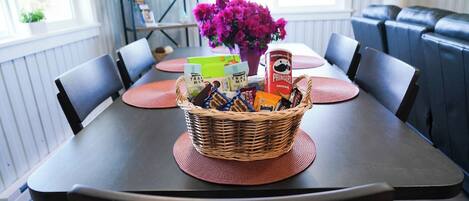 A dining table with a basket of snacks, a vase of flowers, and a bookshelf in the background.