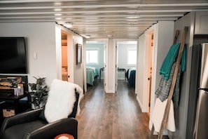 A hallway with a flat-screen TV, a white fluffy chair, and a wooden floor.