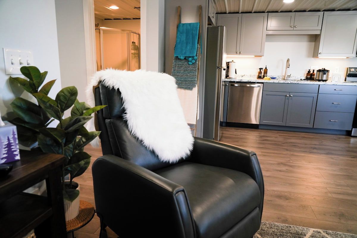 A modern kitchen with grey cabinets, a stainless steel refrigerator, and a wooden floor.