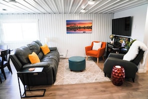 A modern living room with a sofa, armchair, ottoman, and a television mounted on the wall.