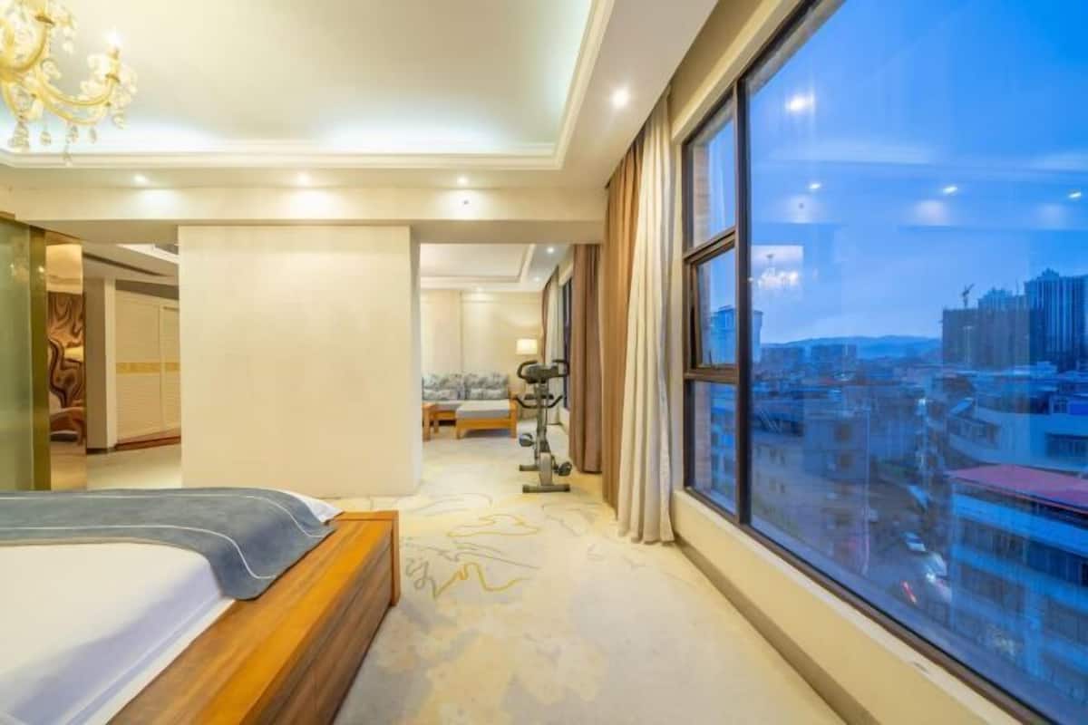 A hotel room with a large bed, exercise equipment, and a city view.