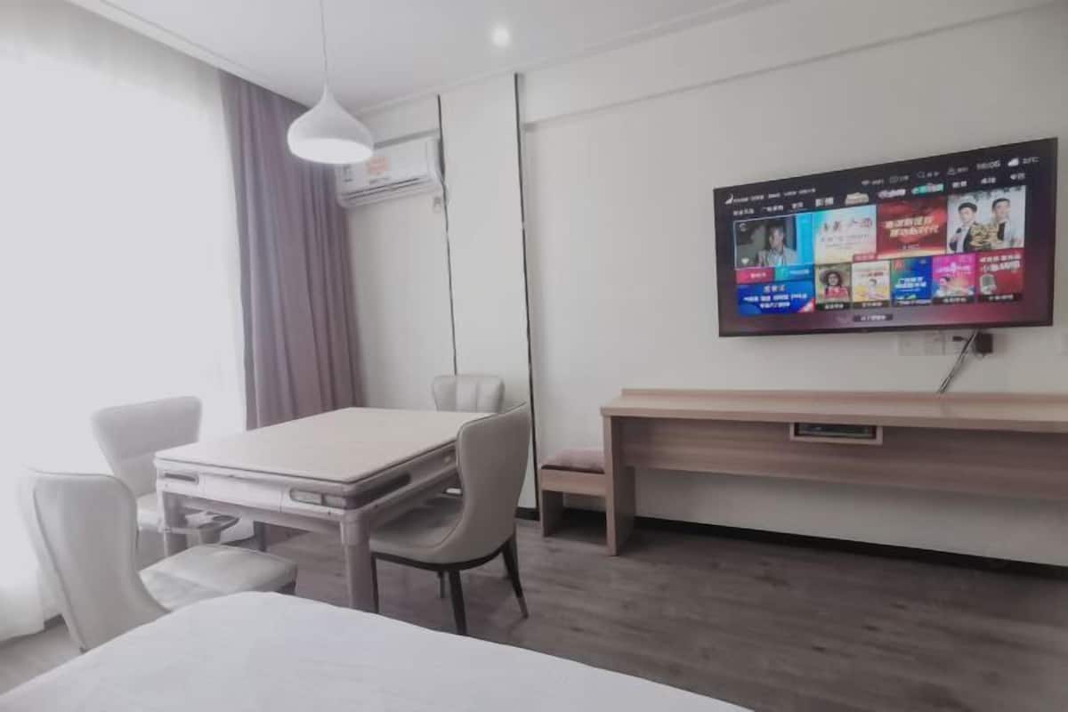 A modern hotel room with a flat-screen TV mounted on the wall, a wooden desk, a comfortable chair, and a small table.