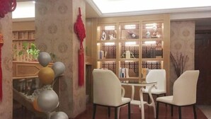 A room with a wooden bookshelf, white chairs, and a small table. - Dc cheng hotel (Beiliu)
