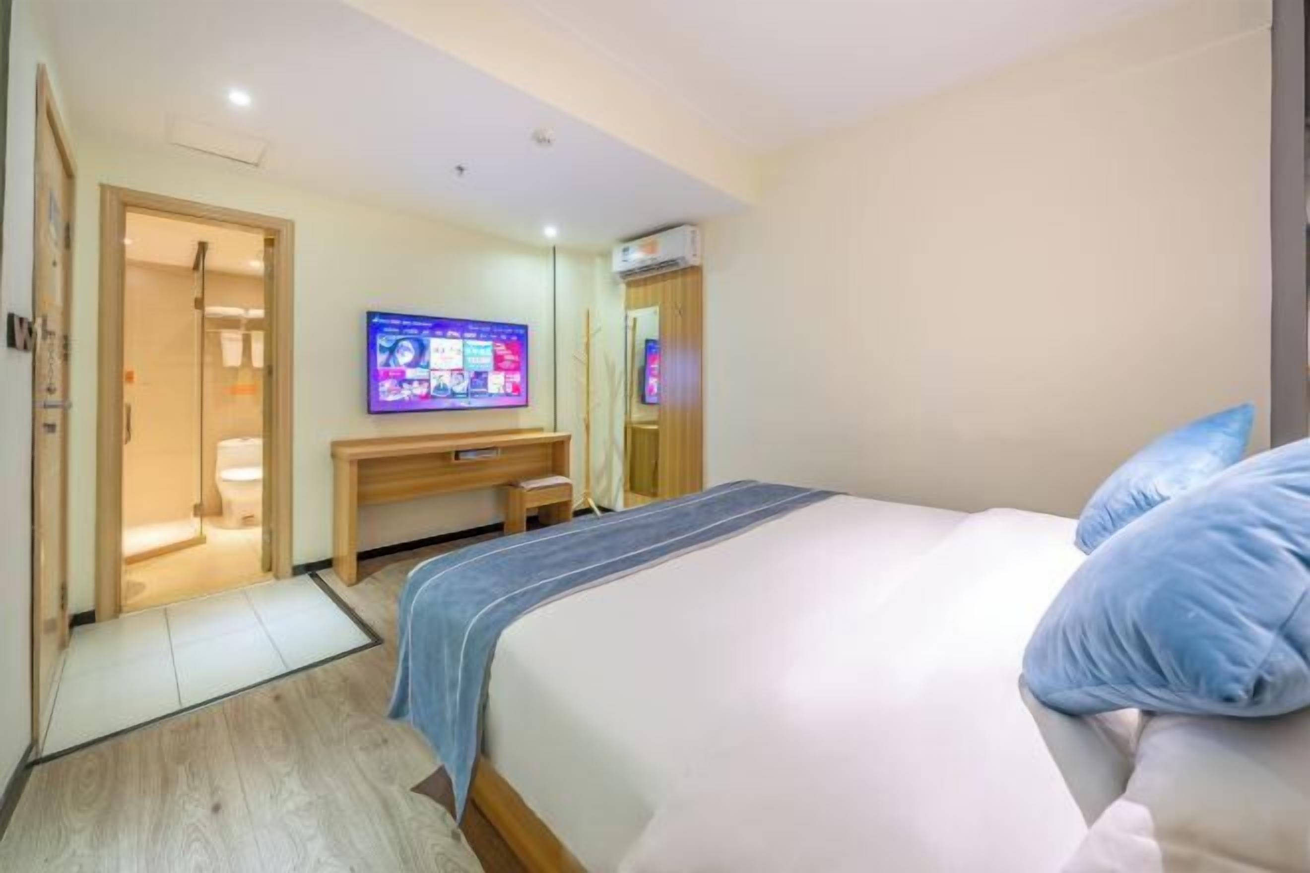 A hotel room with a bed, a desk, a television, and a bathroom visible through an open door.