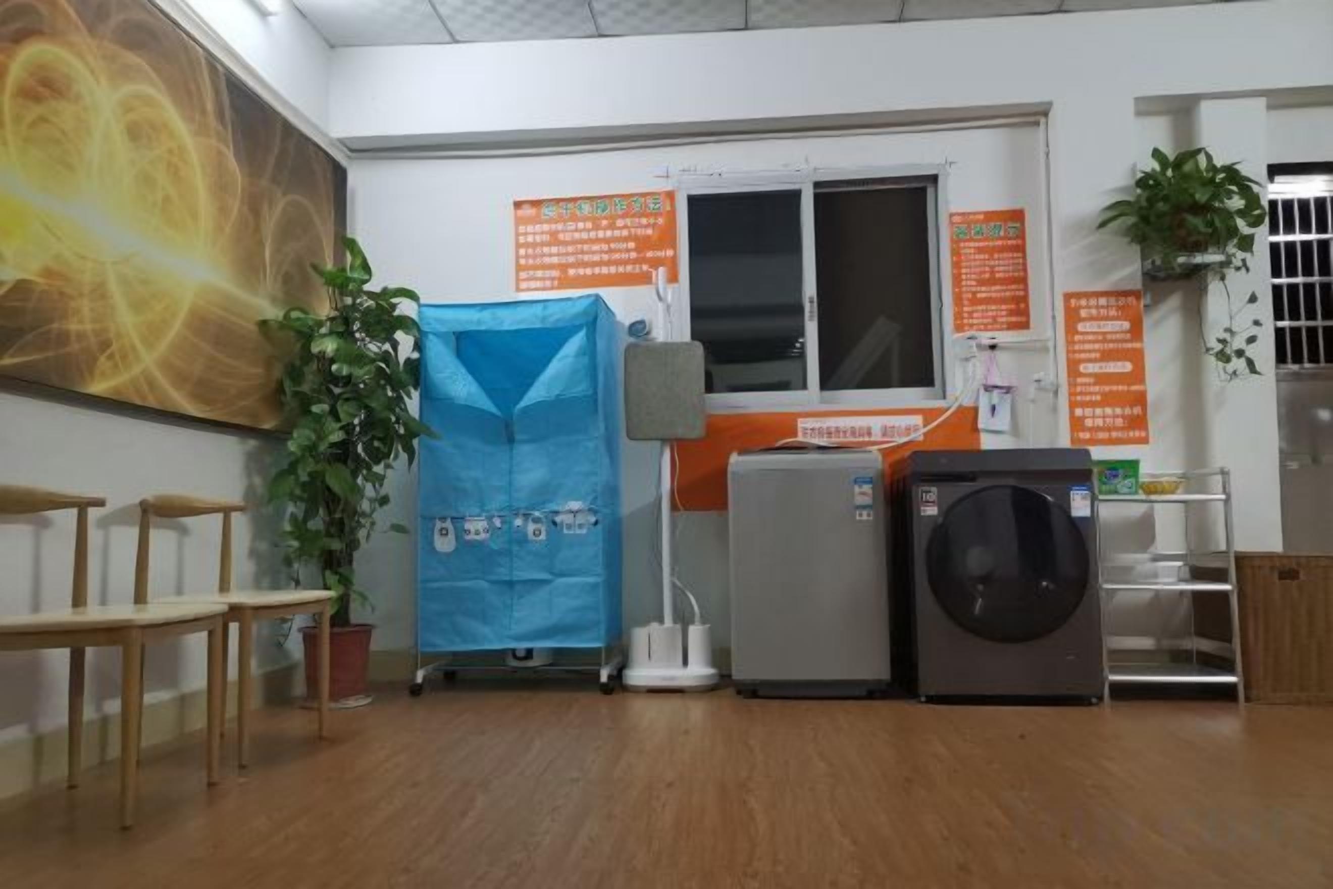 A room with a large painting, a blue covered object, a washing machine, and a refrigerator.