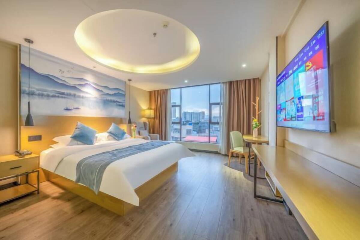 A modern hotel room with a large bed, a desk, and a TV on the wall.