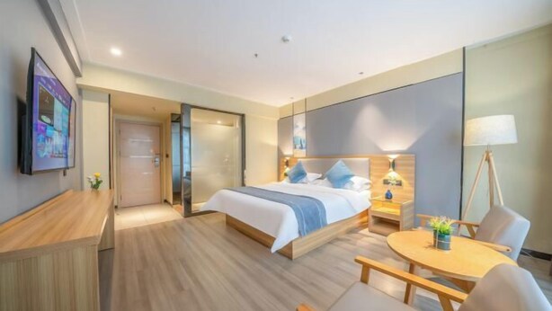 Quarto de hotel com cama, mesa de cabeceira, luminária, cadeira e uma pequena mesa com uma planta.