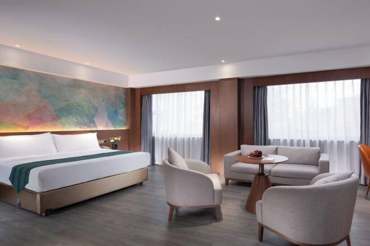 A hotel room with a bed, two armchairs, a small round table, and a large abstract painting on the wall.