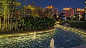A nighttime view of a hotel pool area with water fountains, surrounded by well-maintained greenery and illuminated buildings. - Venus Resort & Restaurant (Chongzuo)