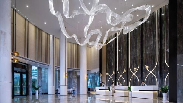 A modern lobby with a glass entrance, a reception desk, and a decorative ceiling sculpture. - Venus Resort & Restaurant (Chongzuo)