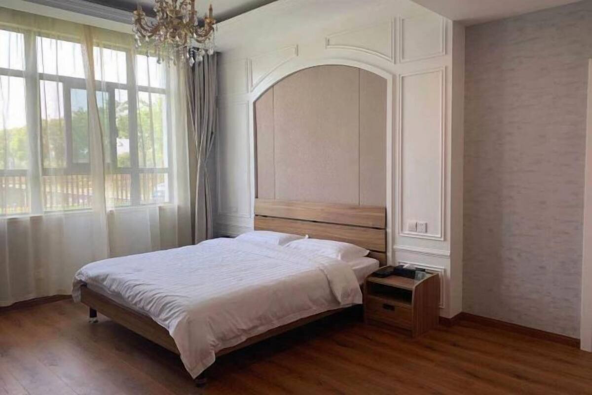 Ein Schlafzimmer mit einem hölzernen Bett, einem Nachttisch, einer Kommode und einem großen Fenster mit Vorhängen.