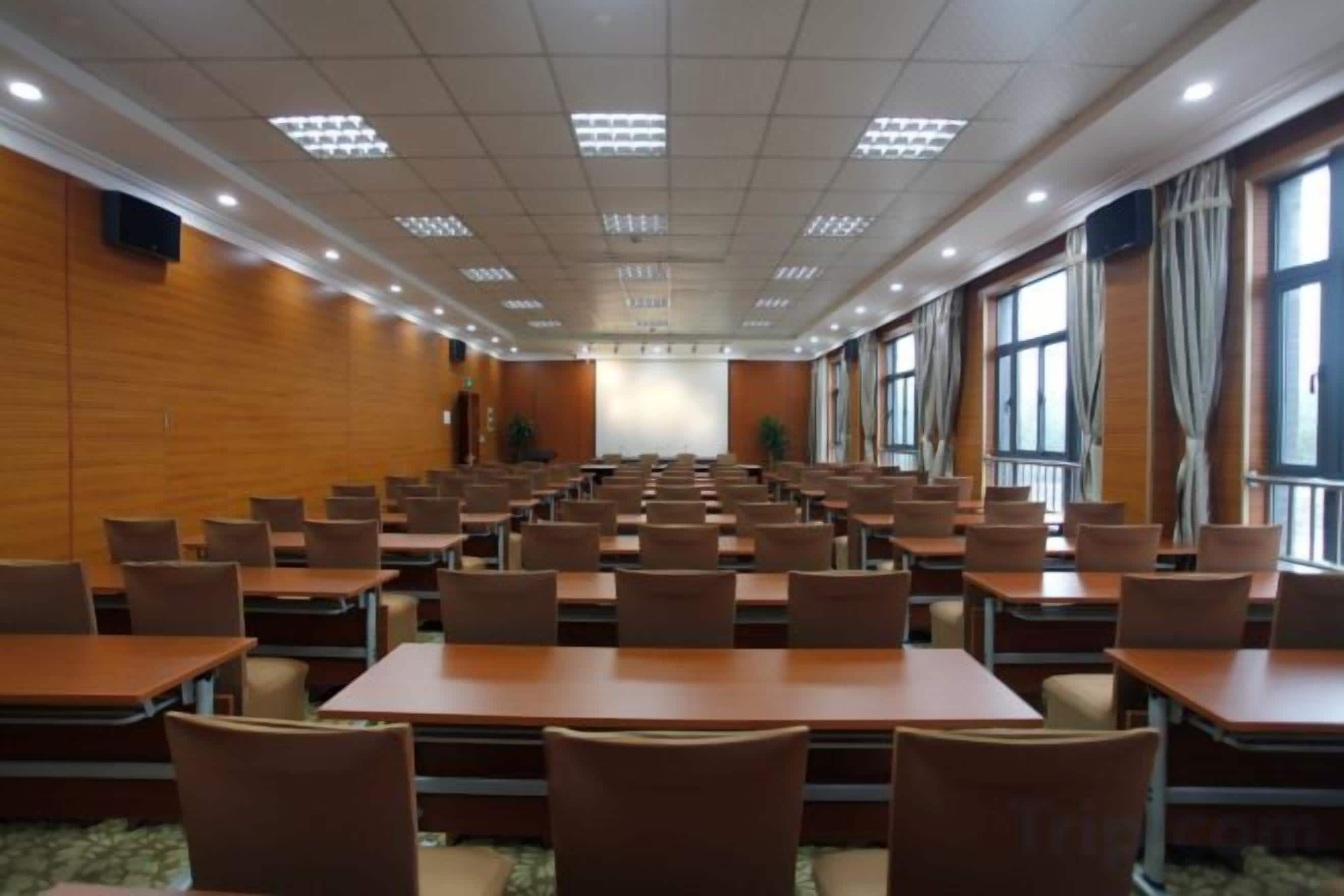 Konferenssitila, jossa on riveissä pöytiä ja tuoleja, suuret ikkunat ja esiintymislava tilan etuosassa.