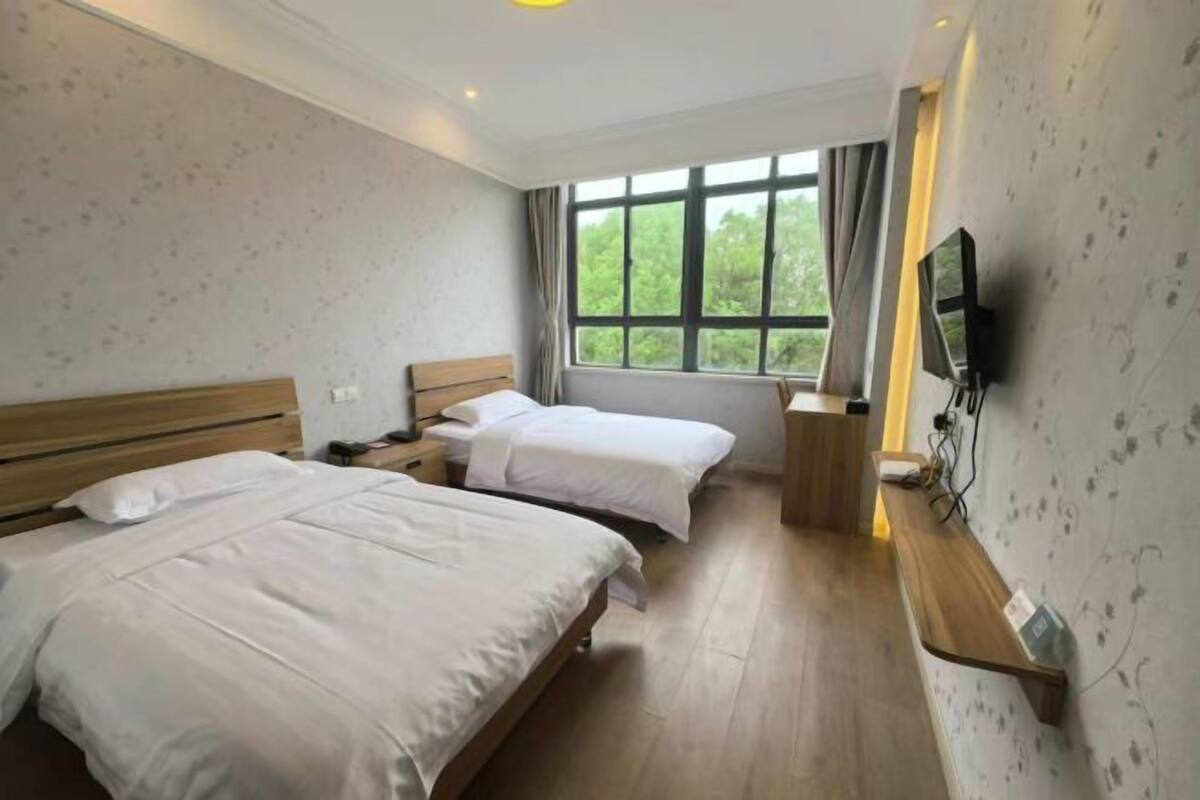 Ein Hotelzimmer mit zwei Betten, einem Fernseher, einem Schreibtisch und einem Fenster mit Blick auf Grünflächen.