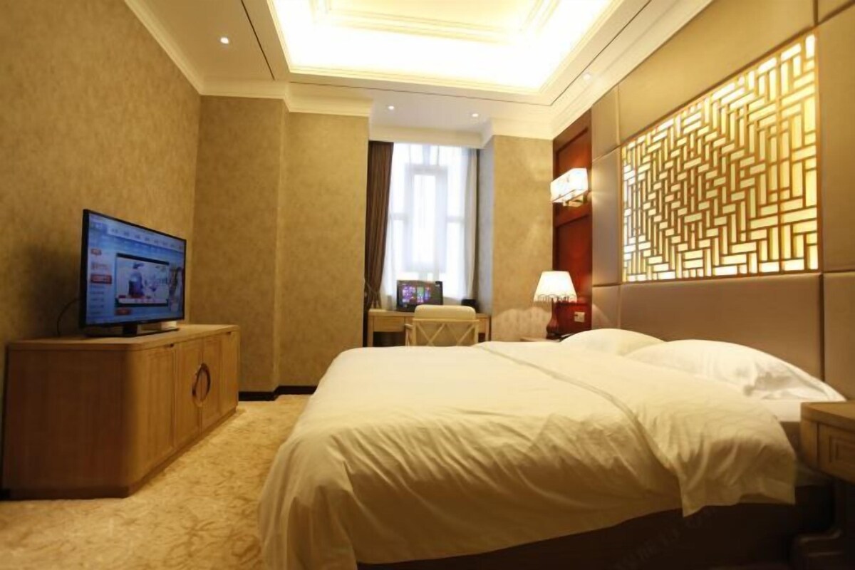 Habitación de hotel con cama, televisión sobre un mueble de madera, escritorio con silla y un panel decorativo en la pared.