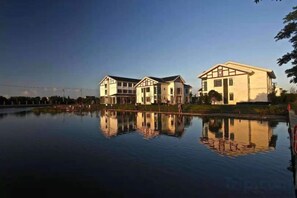 Un edificio reflejado en aguas tranquilas, rodeado de un cielo despejado.