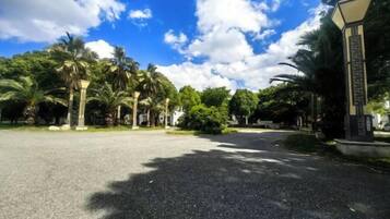 Área pavimentada com palmeiras e um edifício com entrada em colunas.