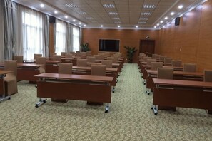Un salón de conferencias con filas de mesas y sillas, una pantalla grande y una puerta al fondo.