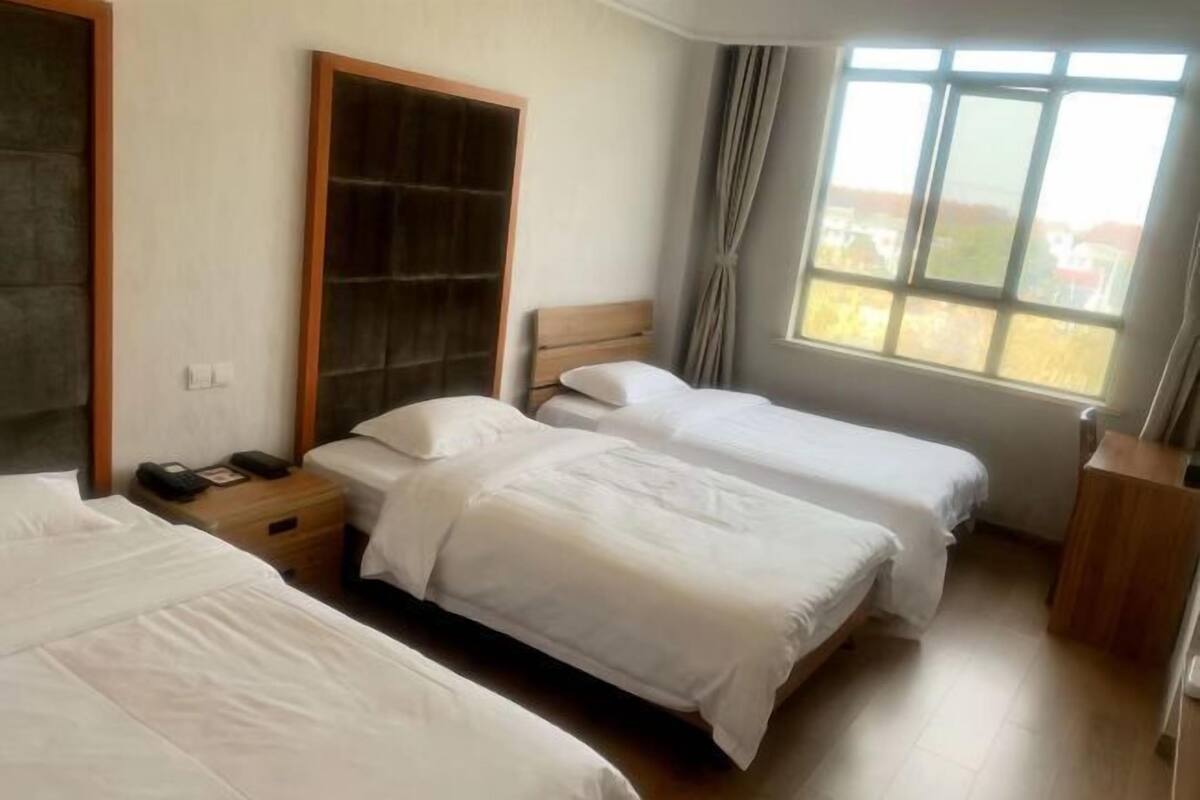 Ein Hotelzimmer mit zwei Einzelbetten, einem Holzschrank, einem Nachttisch mit Telefon und einem Fenster mit Vorhängen.