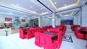 Un hall de hotel con sillas y mesas rojas, una zona de recepción y un cuadro grande en la pared.