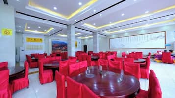 Un salón de conferencias con mesas redondas y sillas rojas, paredes blancas y una pantalla grande.