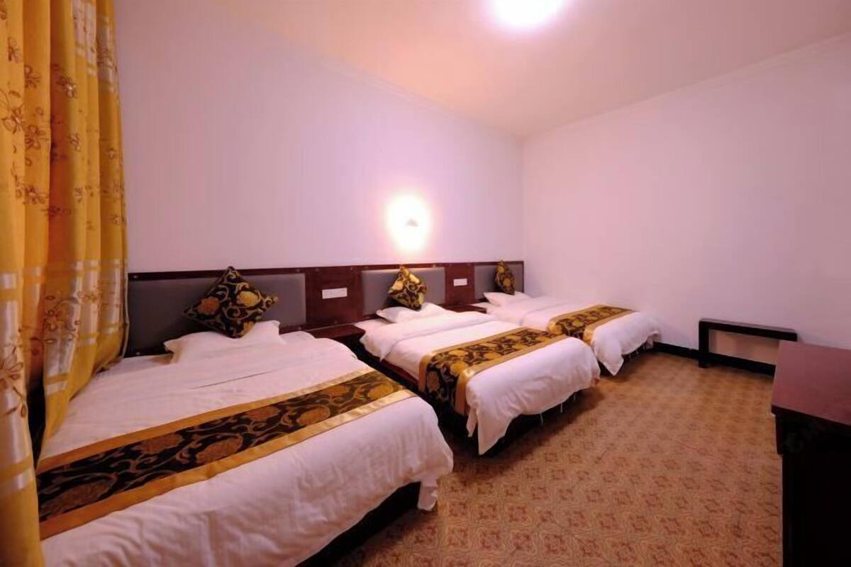 A hotel room with three beds, a bedside table, a lamp, and a patterned carpet.