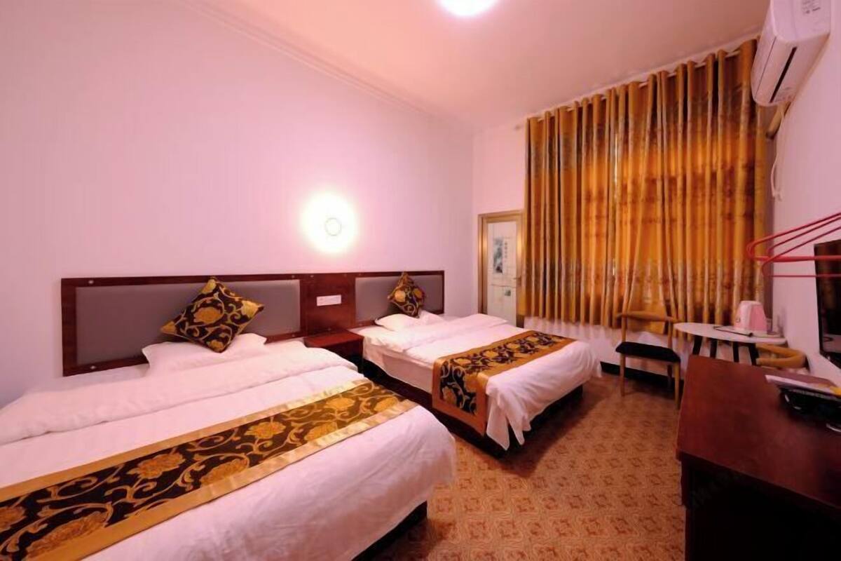 A hotel room with two beds, a desk, a chair, a lamp, and a window with curtains.