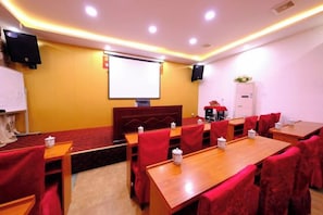 Un salón de conferencias con una pantalla grande, varias mesas y sillas rojas.