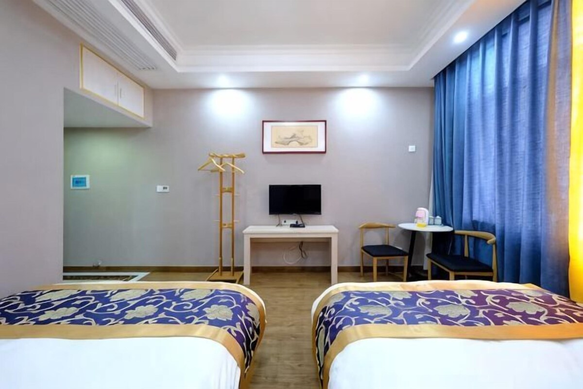 Habitación de hotel con dos camas, un escritorio con televisor, una silla y una ventana con cortinas.