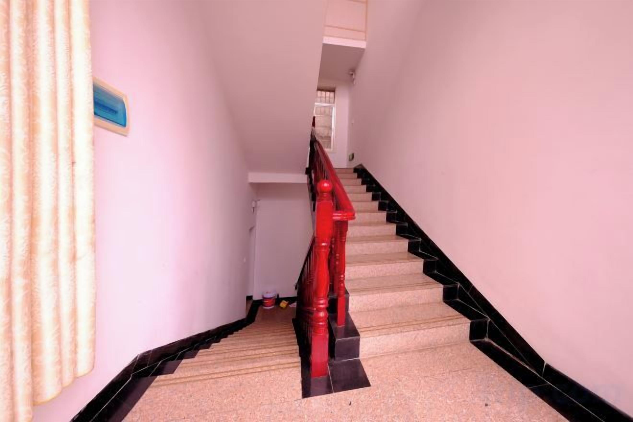 Una escalera con barandilla roja y detalles negros en el borde, que lleva a una plataforma con un letrero azul.
