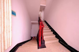 Una escalera con barandilla roja y detalles negros en el borde, que lleva a una plataforma con un letrero azul.