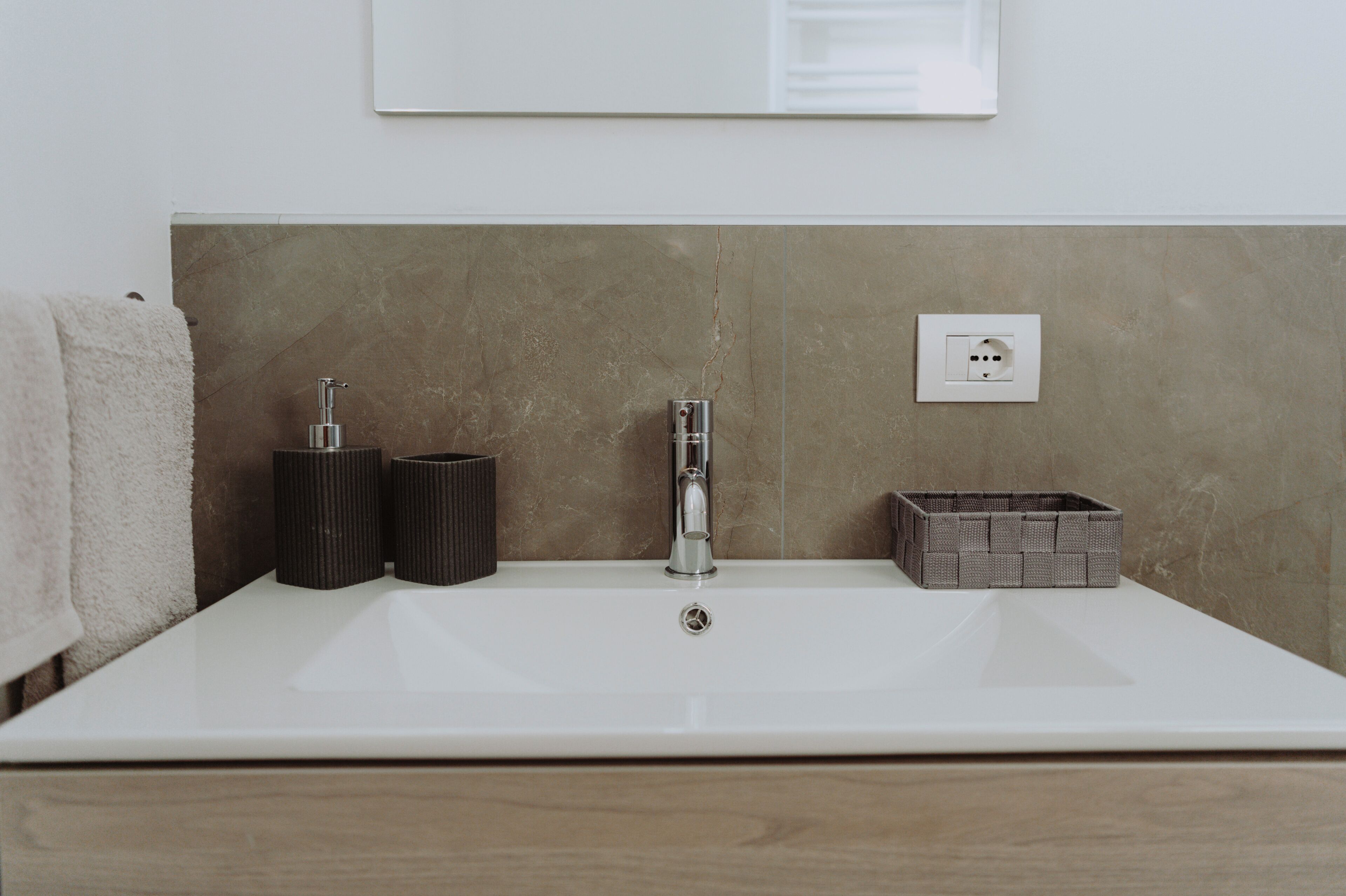 A bathroom with a white sink, a towel, two black cylindrical containers, and a gray woven basket.