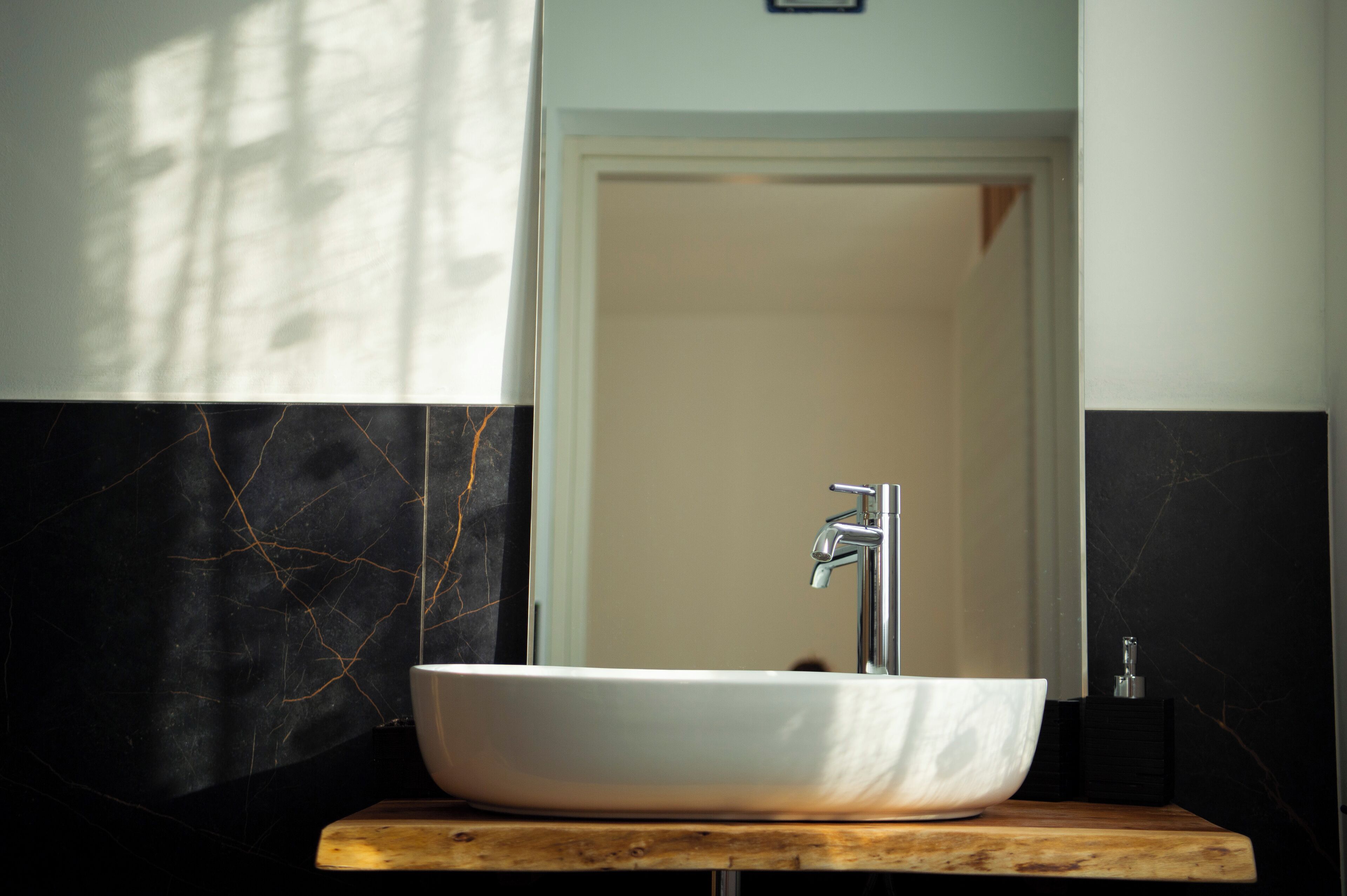 Un baño con un lavabo blanco sobre encimera de madera, un grifo moderno y una pared de mármol con grietas.