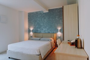 Un dormitorio moderno con cama, lámparas de noche, cafetera y una pared grande de acento azul.